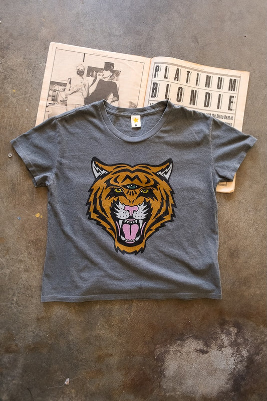 Vintage black t-shirt with a tiger graphic on a textured surface with a magazine underneath.