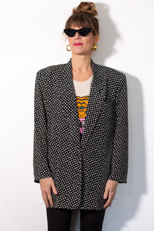 Woman wearing a black and white patterned blazer with a colorful top underneath on a white background