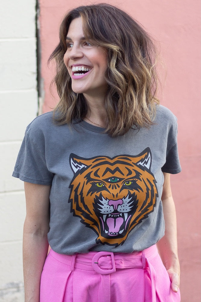 Woman wearing a gray t-shirt with a tiger graphic design against a pink wall.