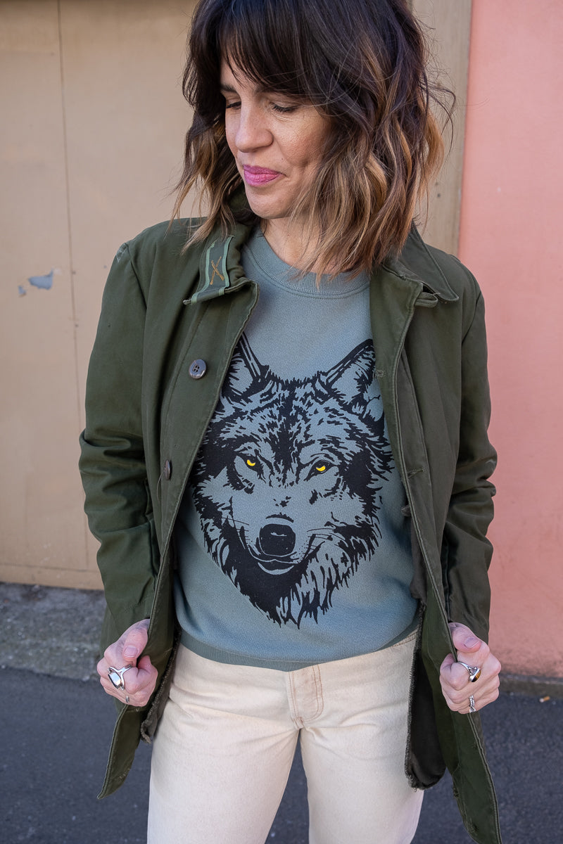 Thread Hippie green women's sweatshirt styled with vintage military jacket and white jeans.