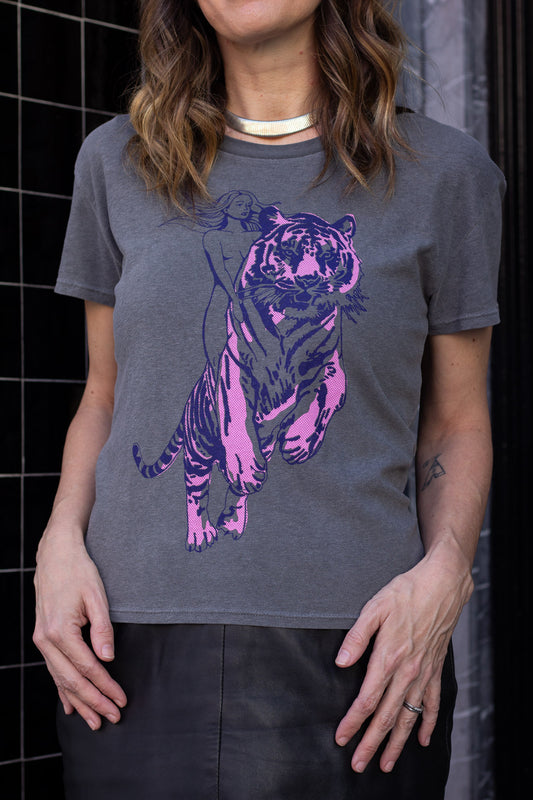 Woman wearing a gray t-shirt with a purple tiger design against a black tiled wall.