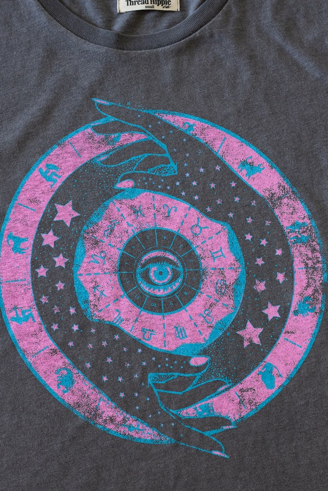Close-up of Zodiac novelty tee print in neon pink and blue on vintage black fabric.