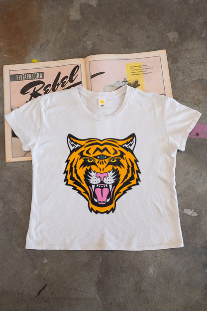 White t-shirt with a tiger graphic on a gray surface with a magazine underneath