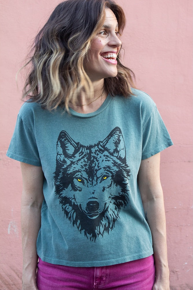 Woman wearing a green t-shirt with a wolf graphic against a pink background