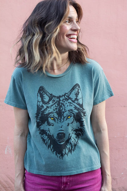 Woman wearing a green t-shirt with a wolf graphic against a pink background