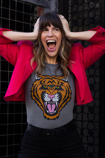 Woman wearing a black t-shirt with a tiger graphic and a red jacket, standing against a dark textured wall.