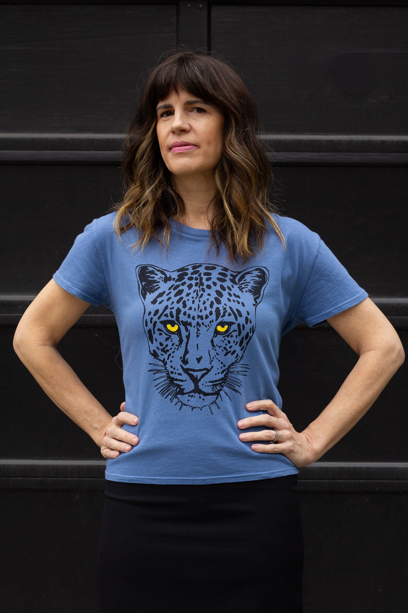 Woman wearing a blue t-shirt with a leopard graphic against a black background in the city.