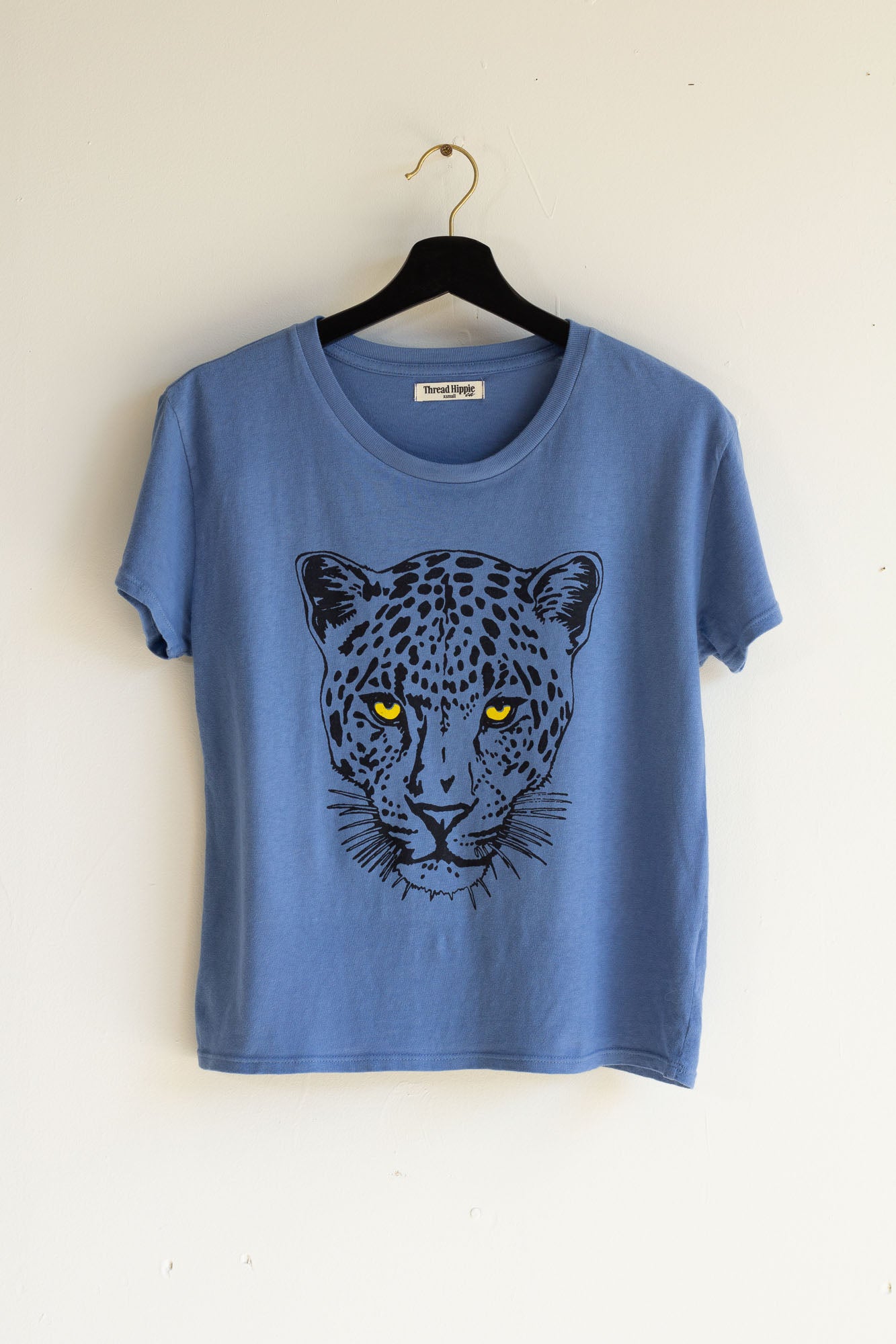 Blue women's t-shirt with a leopard graphic on a hanger against a white background.
