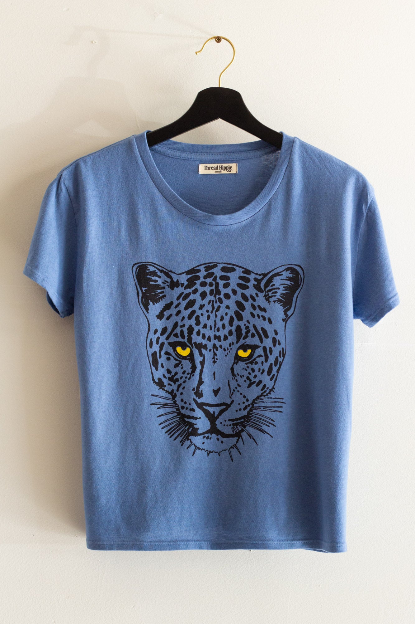 Blue t-shirt with a leopard graphic on a hanger against a white background.