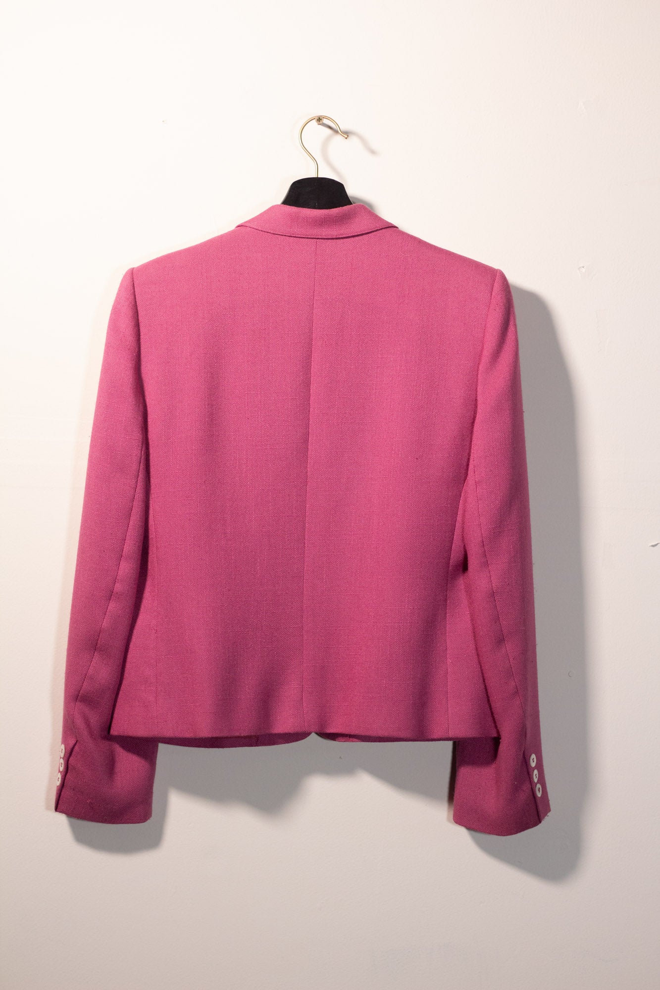 Pink blazer on a hanger against a white wall