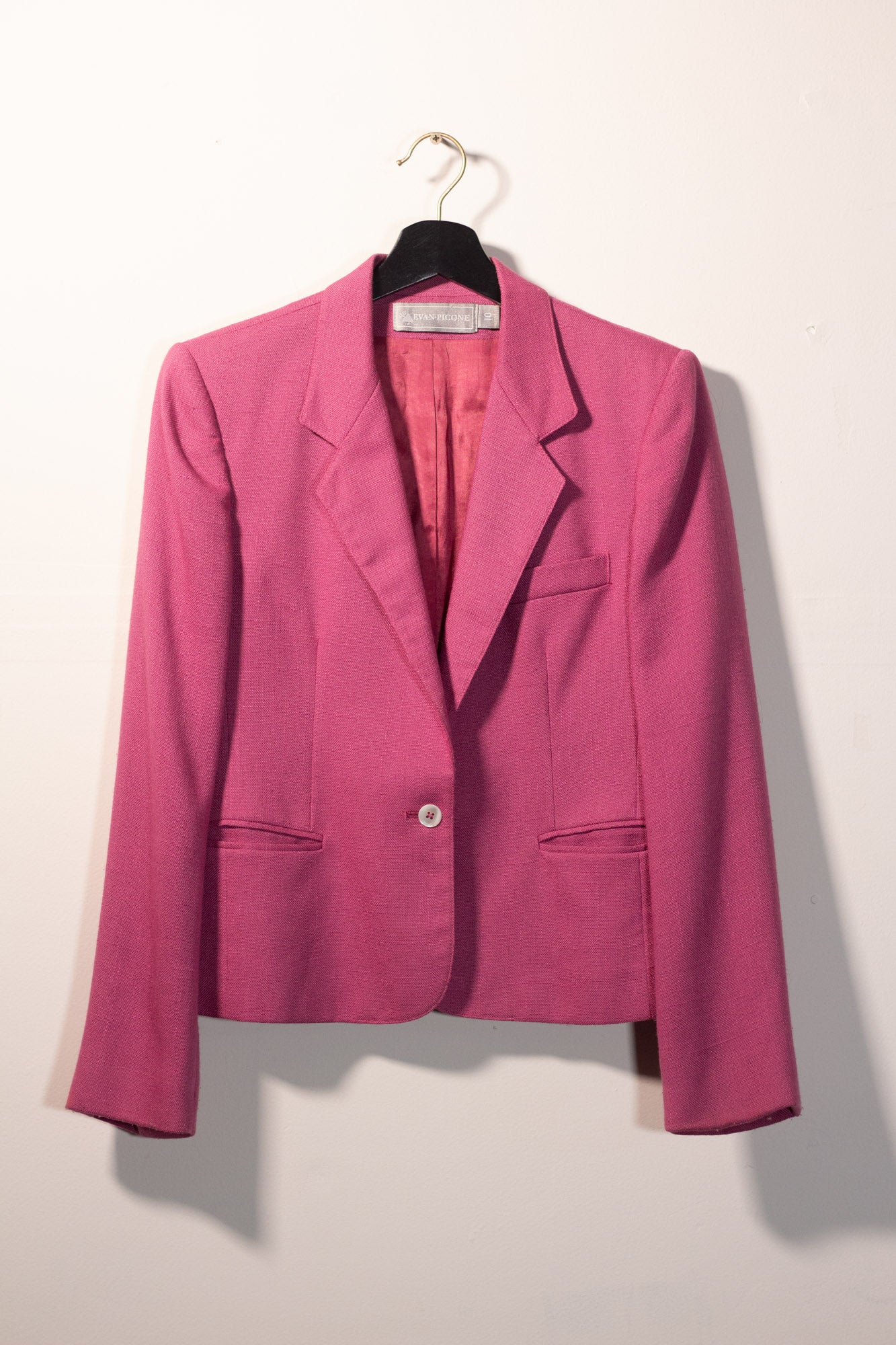 Pink blazer on a hanger against a white background
