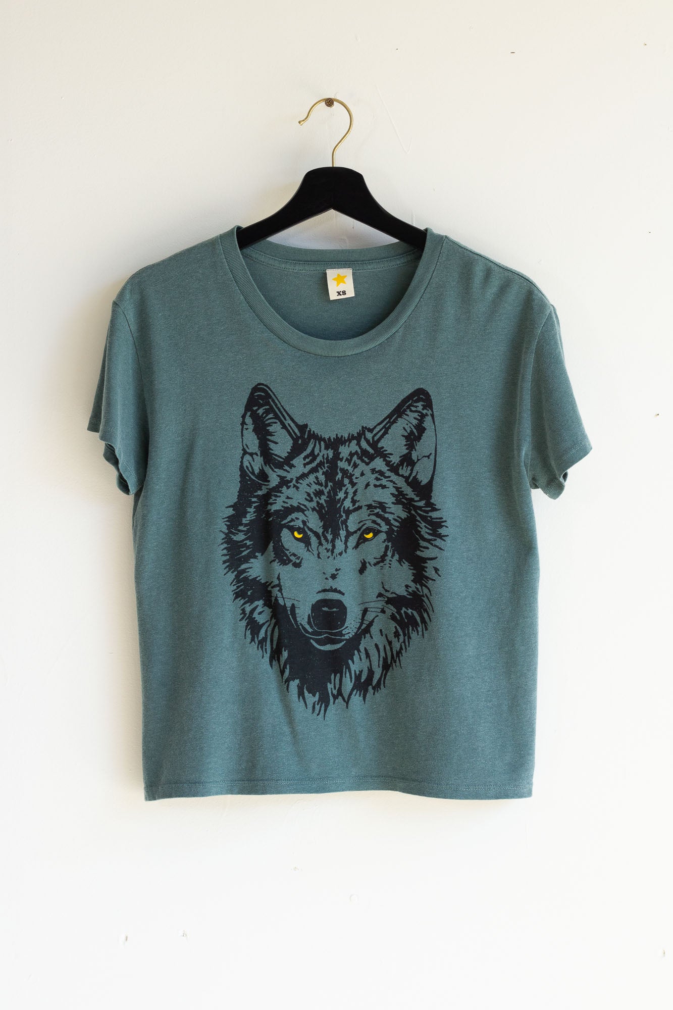 Green women's t-shirt with a wolf graphic on a hanger against a white background.