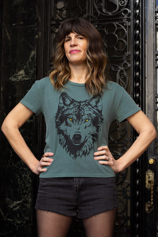 Woman wearing a green t-shirt with a wolf graphic in front of an ornate black door.