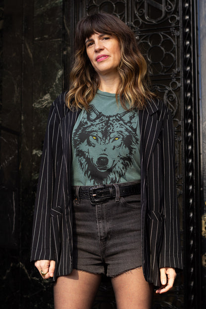 Woman wearing a green graphic t-shirt with a wolf, styled with a vintage black blazer design in front of an ornate door.