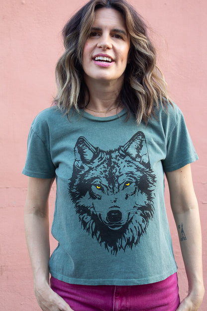 Woman wearing a green tshirt with a wolf graphic against a pink background.
