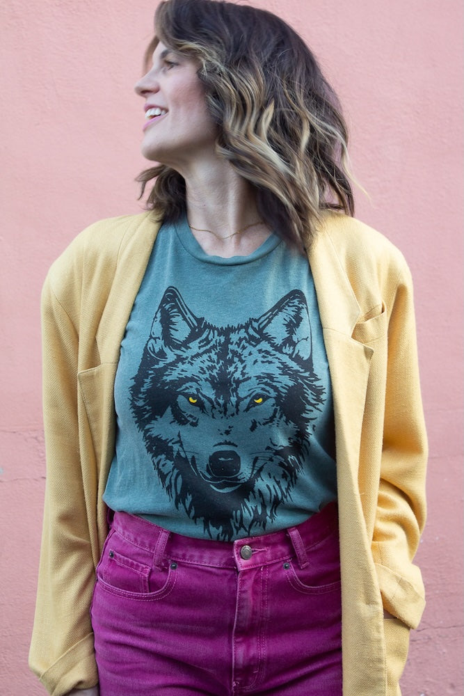 Woman wearing a green t-shirt with a wolf graphic against a pink background.