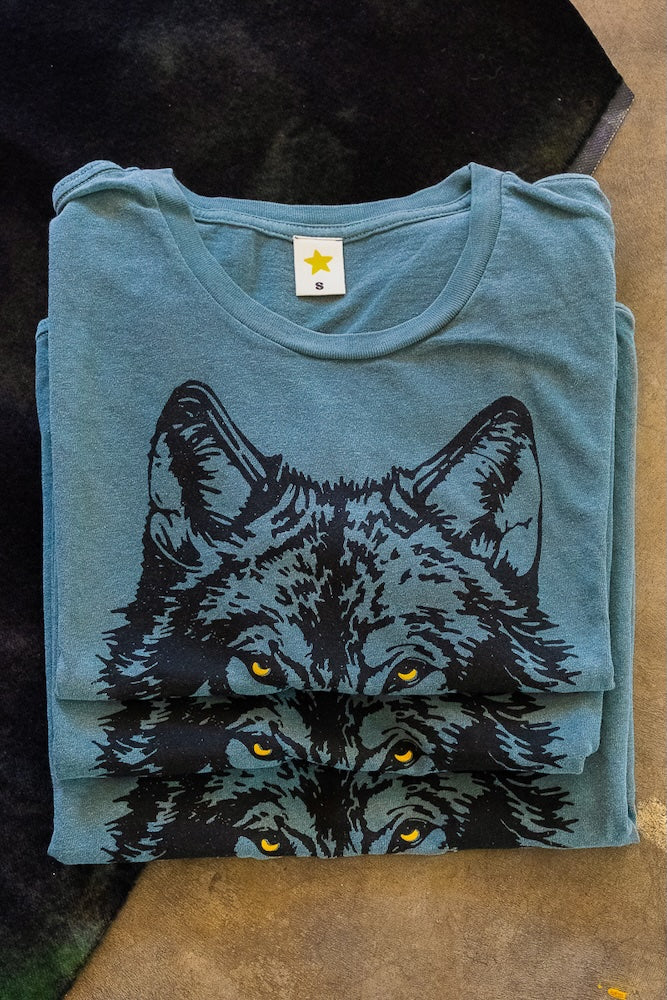 Folded stack of green t-shirts with a wolf graphic on a textured surface.