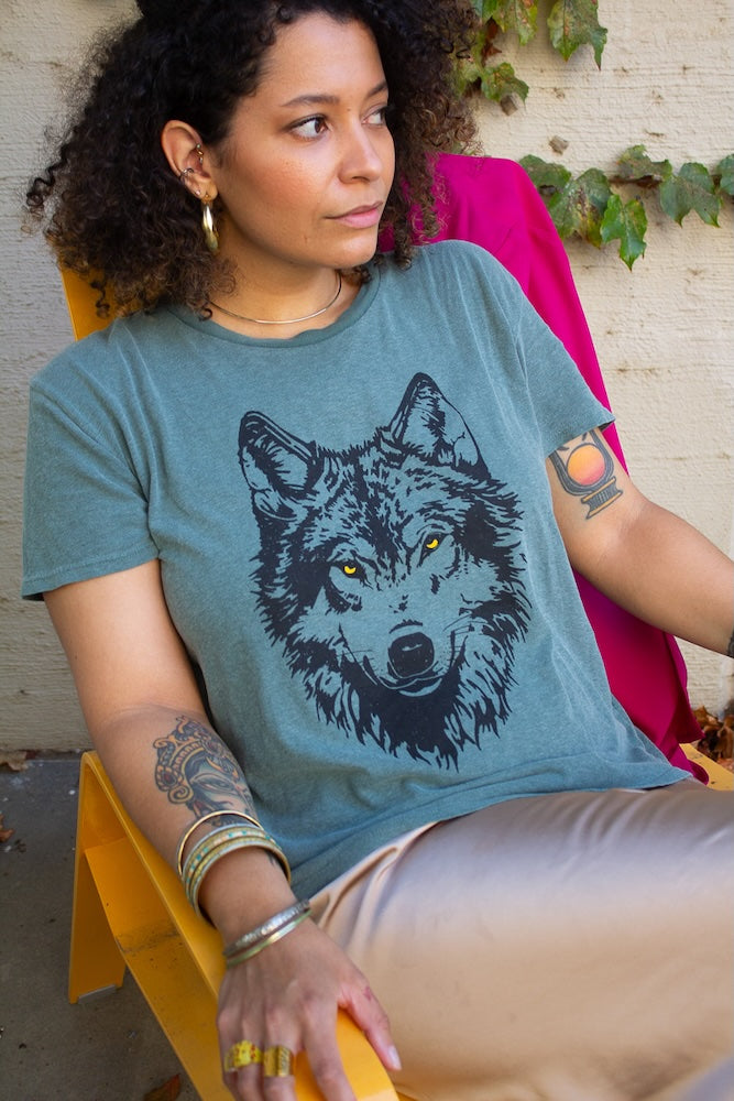 Woman wearing a green t-shirt with a wolf graphic, sitting outdoors.