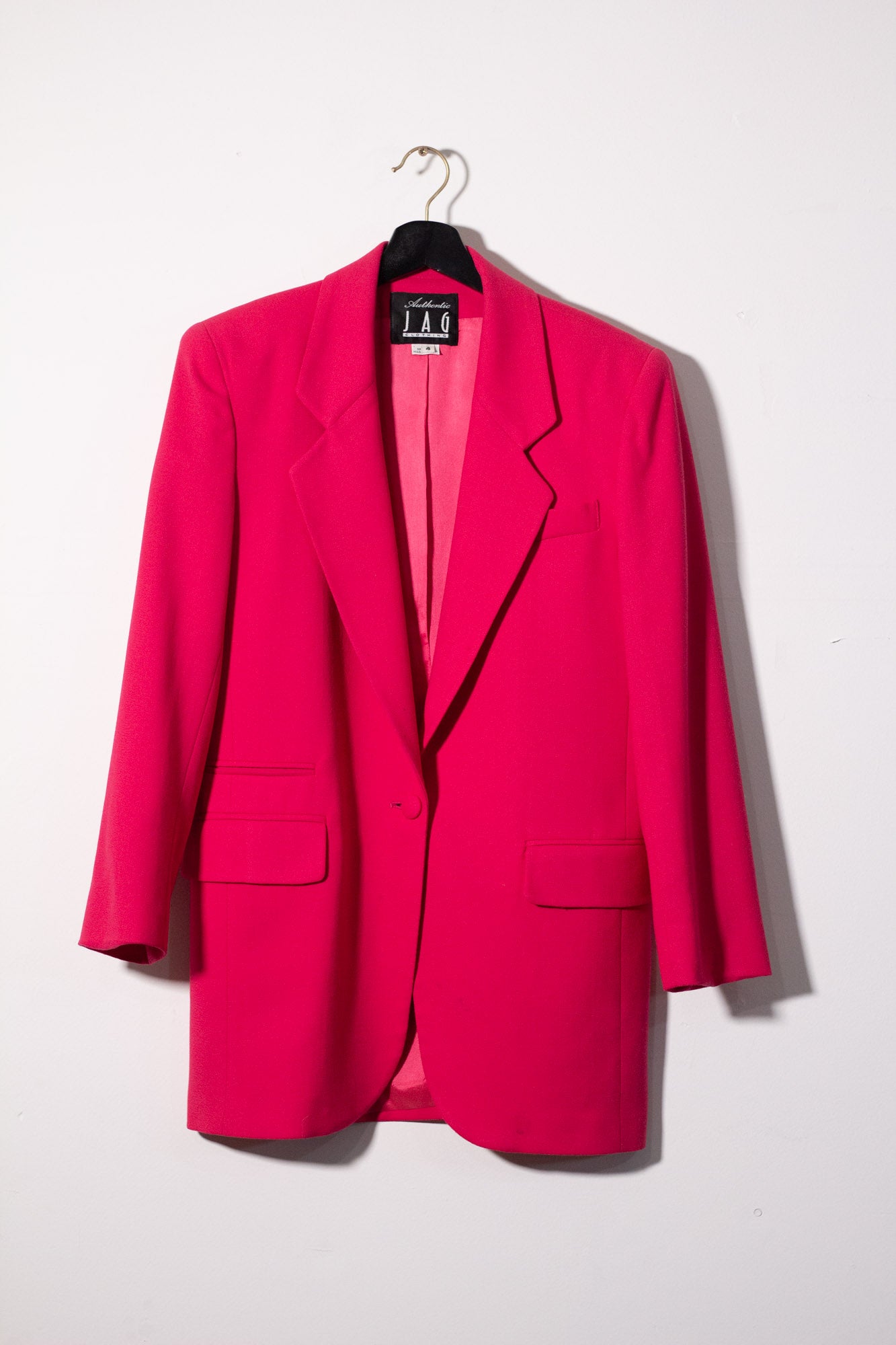Bright pink blazer on a hanger against a white background