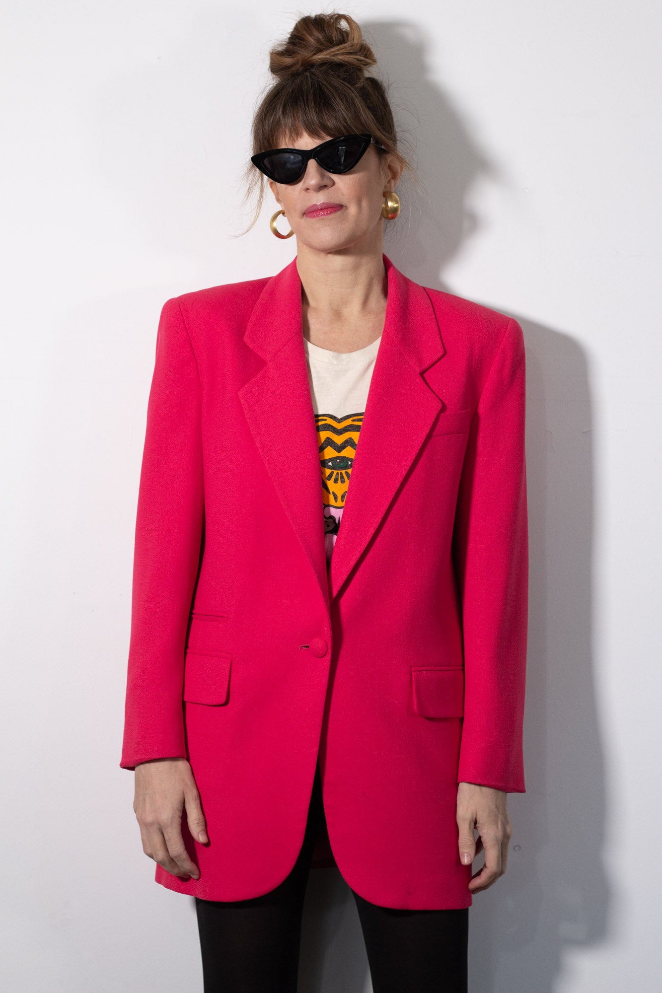 Person wearing a bright pink blazer over a graphic t-shirt against a white background