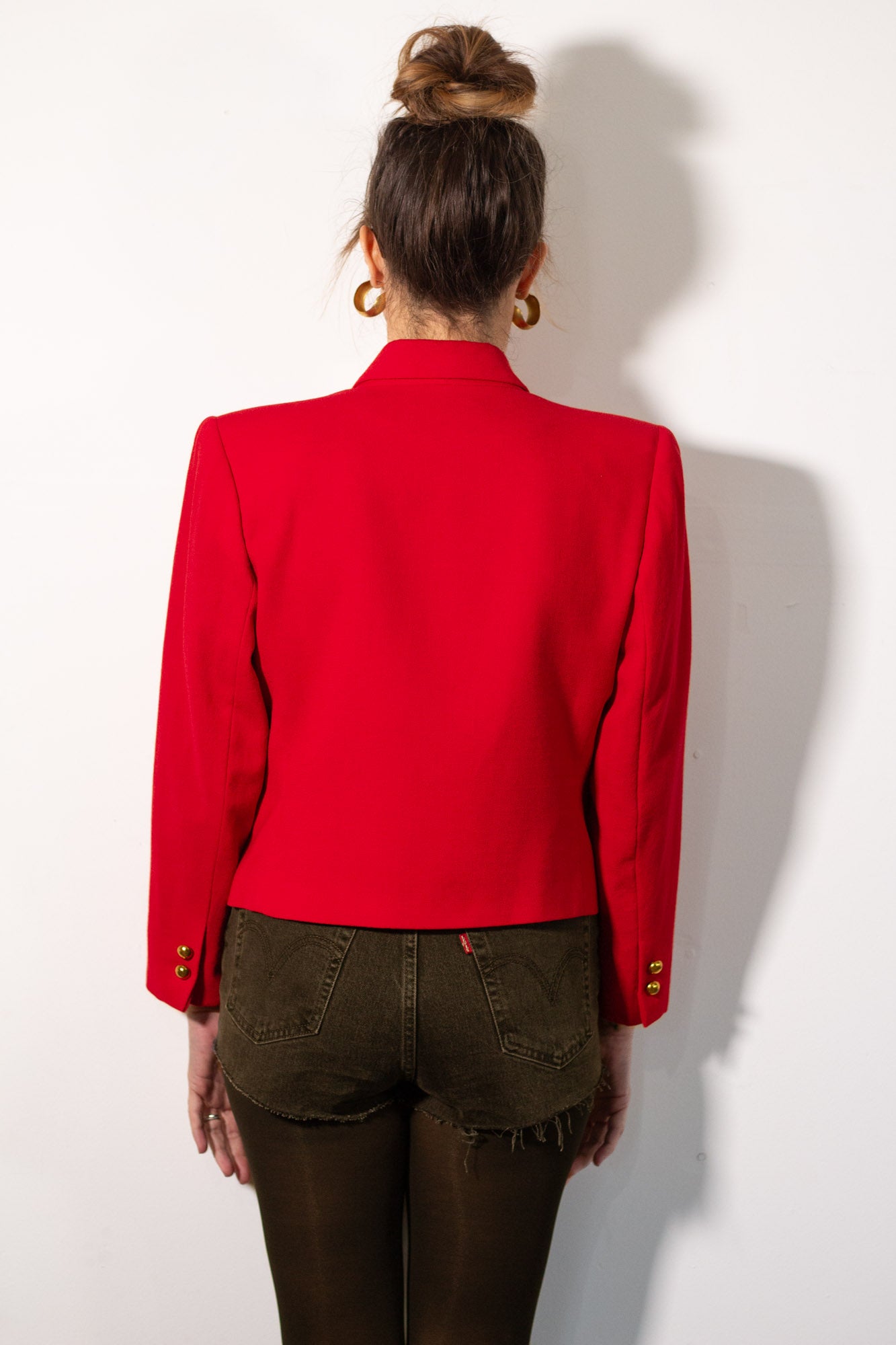 Person wearing a red blazer and brown pants against a white background