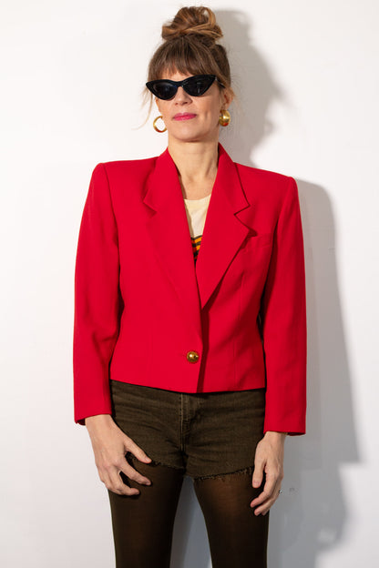 Person wearing a red blazer and sunglasses against a white background