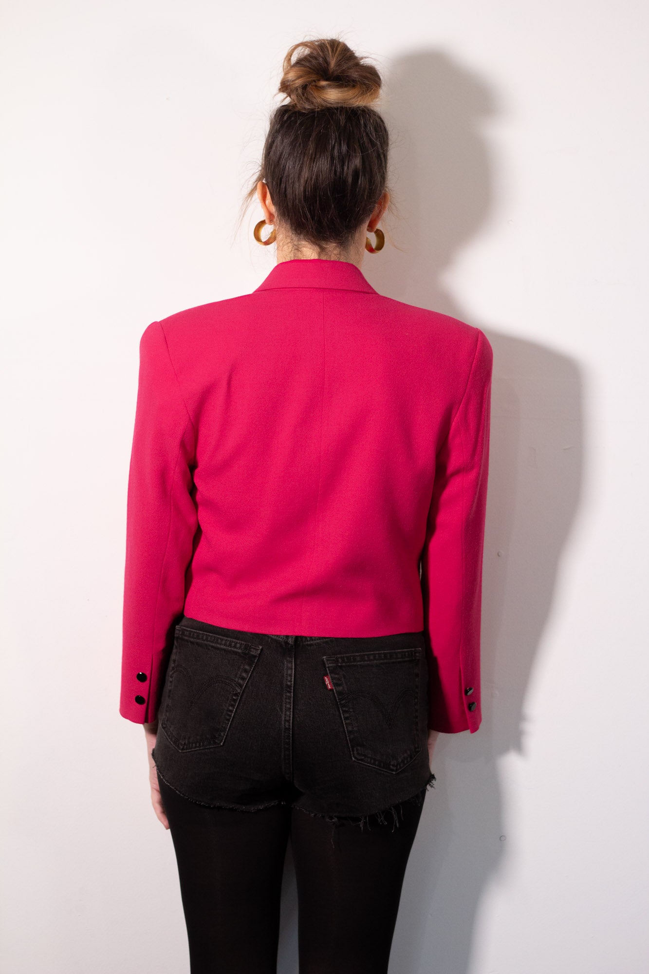 Person wearing a bright pink jacket and black pants against a white background