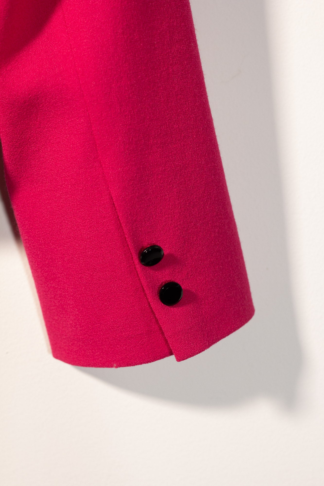 Close-up of a bright pink blazer with black buttons on a light background