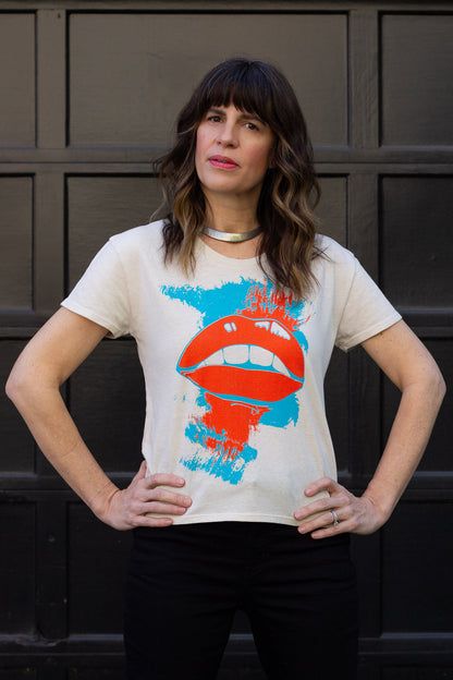 Woman wearing a t-shirt with a graphic design of red lips and blue paint splashes against a dark background.