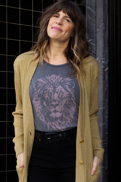 Woman wearing a gold cardigan over a graphic t-shirt with a lion design against a tiled wall.