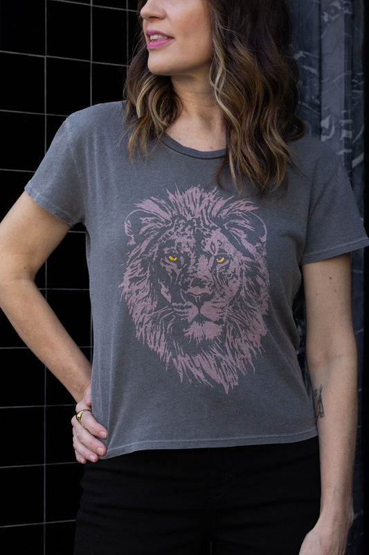 Woman wearing a black t-shirt with a lion graphic design against a black tiled wall.