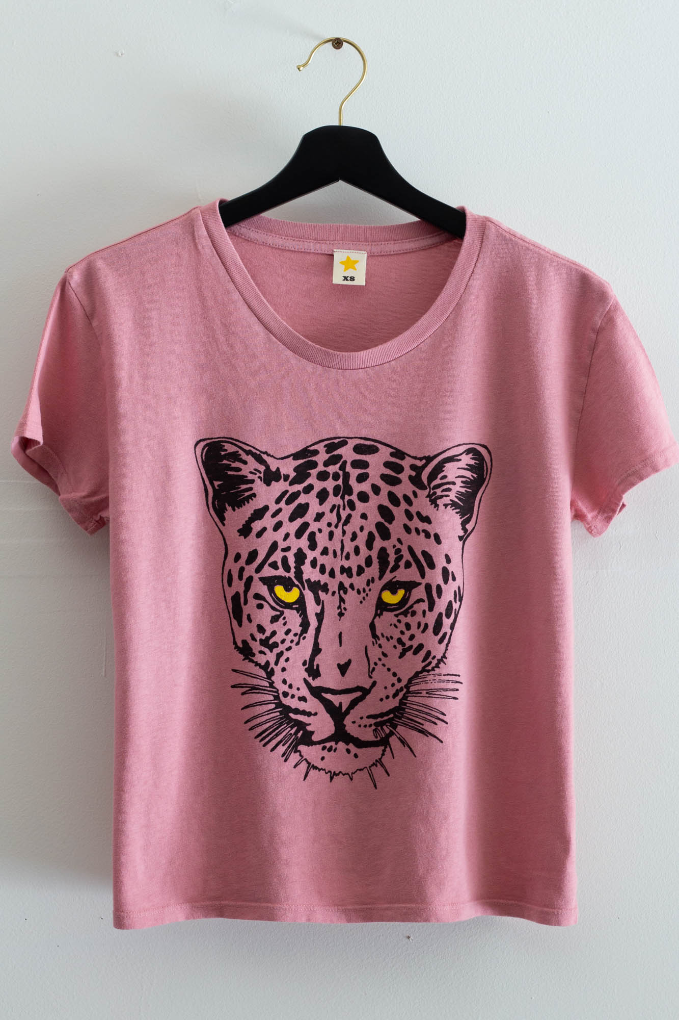 Pink t-shirt with a leopard graphic on a hanger against a white background