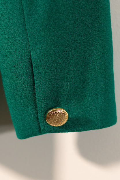 Close-up of a green coat with a gold button on a neutral background