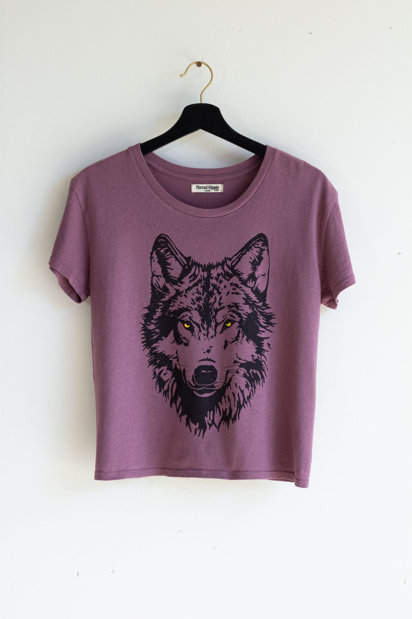 Purple t-shirt with a wolf graphic on a hanger against a white background.