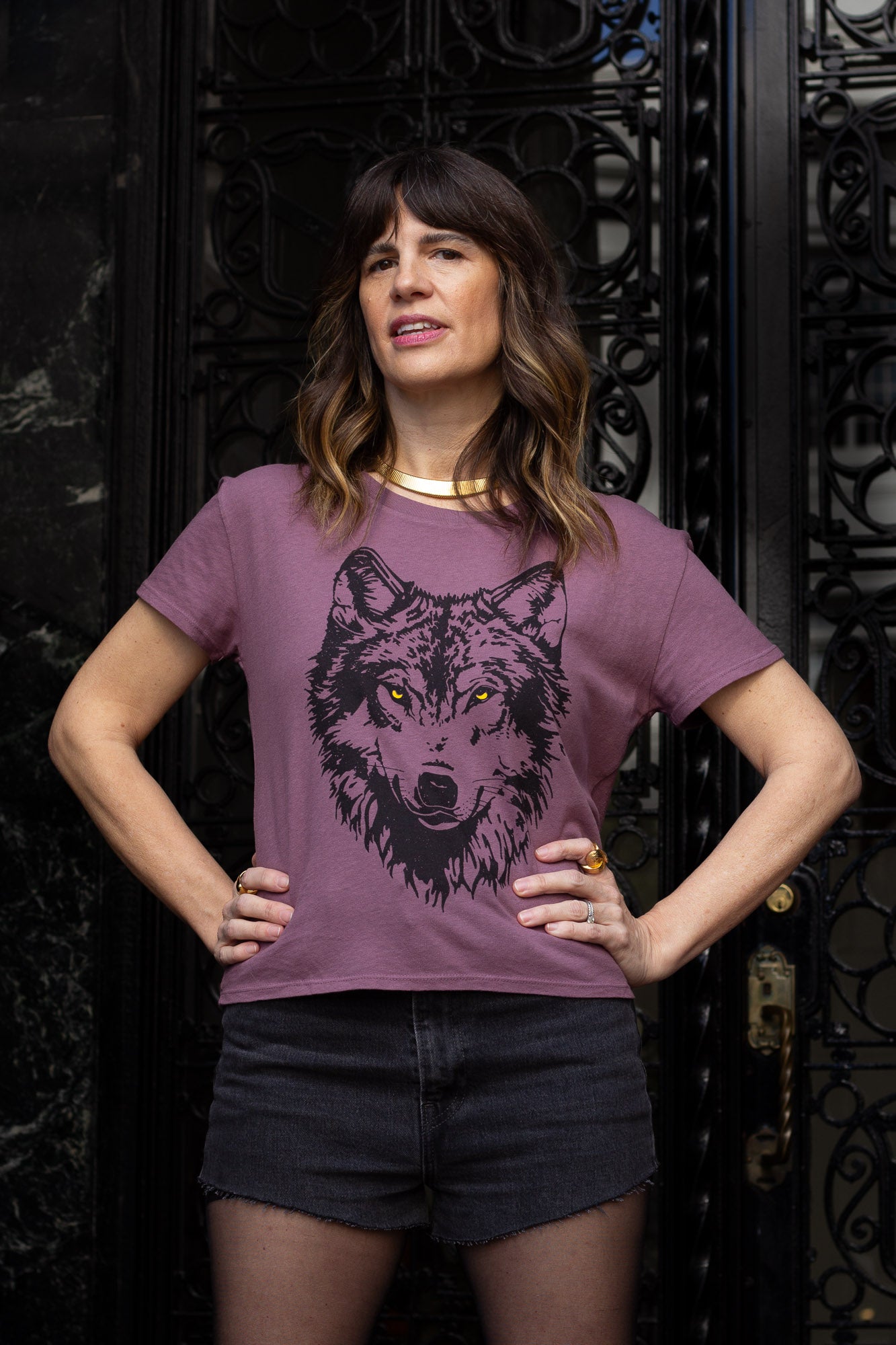 Woman wearing a purple t-shirt with a wolf graphic design in front of an ornate black gate.
