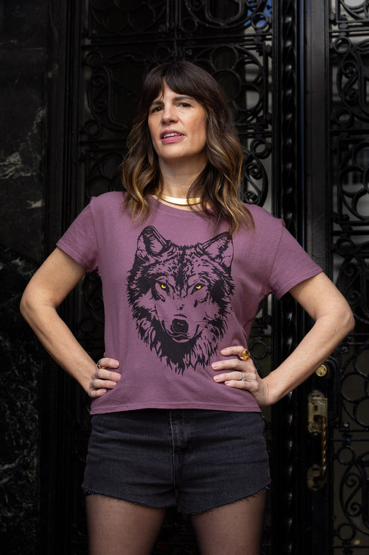 Woman wearing a purple t-shirt with a wolf graphic design in front of an ornate black gate.