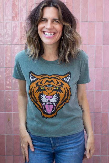 Woman wearing a green tiger tee with a against a pink tiled wall.