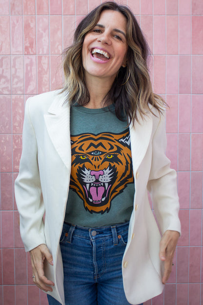 Smiling woman wearing a graphic tee with a tiger design against a pink tiled wall.