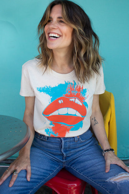 Woman wearing the thread hippie she says graphic t-shirt sitting against a teal wall.