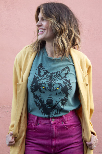Woman wearing a vintage green t-shirt with a wolf graphic and a yellow cardigan against a pink background.