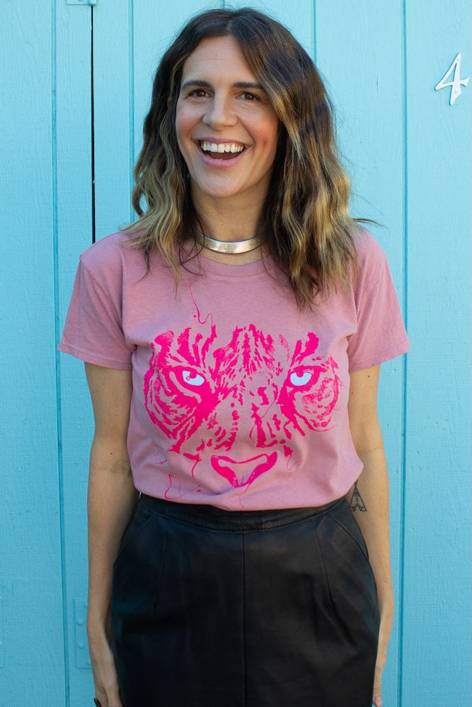 Angela wearing women's pink t-shirt with tiger eyes graphic on blue wall.