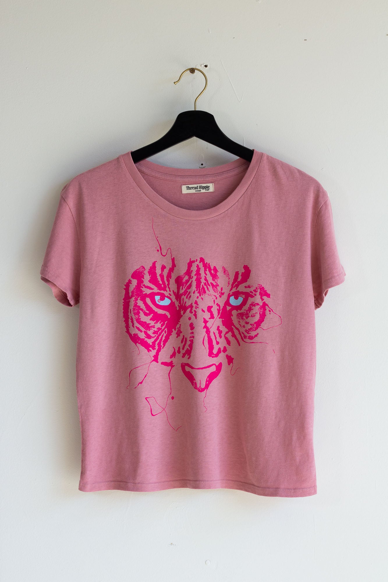 Pink women's tiger t-shirt on a hanger against a white wall.