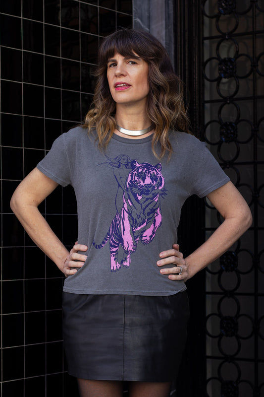 Woman wearing a gray t-shirt with a purple tiger design against a black tiled wall.