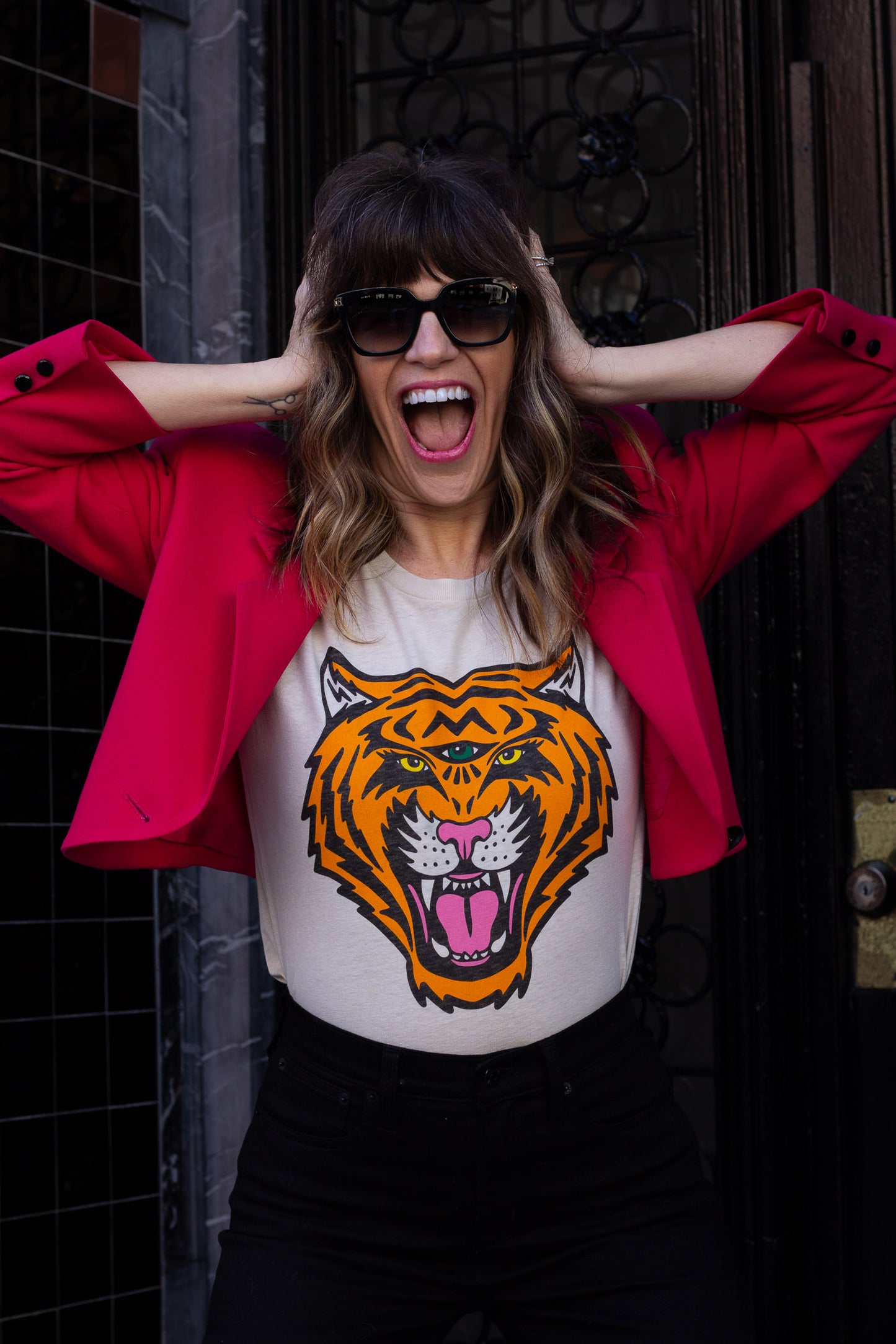 Woman wearing a white t-shirt with a tiger graphic and a red jacket, standing against a dark background.