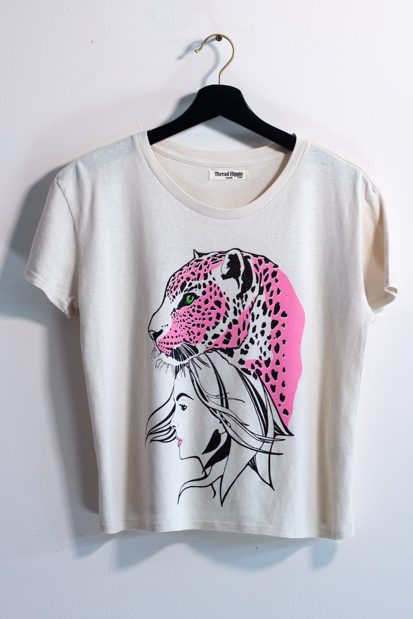 White t-shirt with pink and black leopard design on a hanger against a white background.