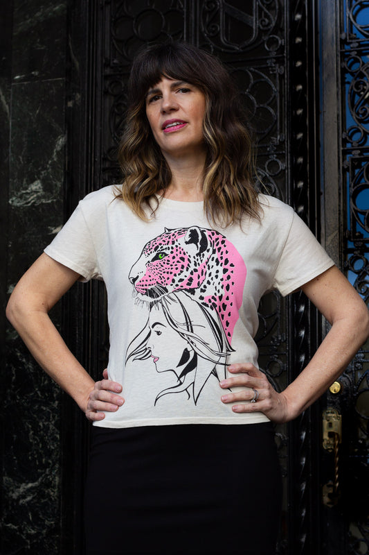 Woman wearing a white t-shirt with a graphic design of a woman's face and a pink panther, standing against a dark background.