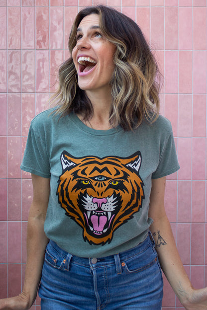 Woman wearing a Thread Hippie tee shirt with a tiger graphic against a pink tiled wall.