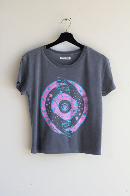 Gray t-shirt with a zodiac design on a hanger against a white wall.